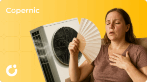 Kobieta siedząca na fotelu, spocona przez wysoką temperaturę, wachlująca się. Za kobietą pompa ciepła powietrze-powietrze